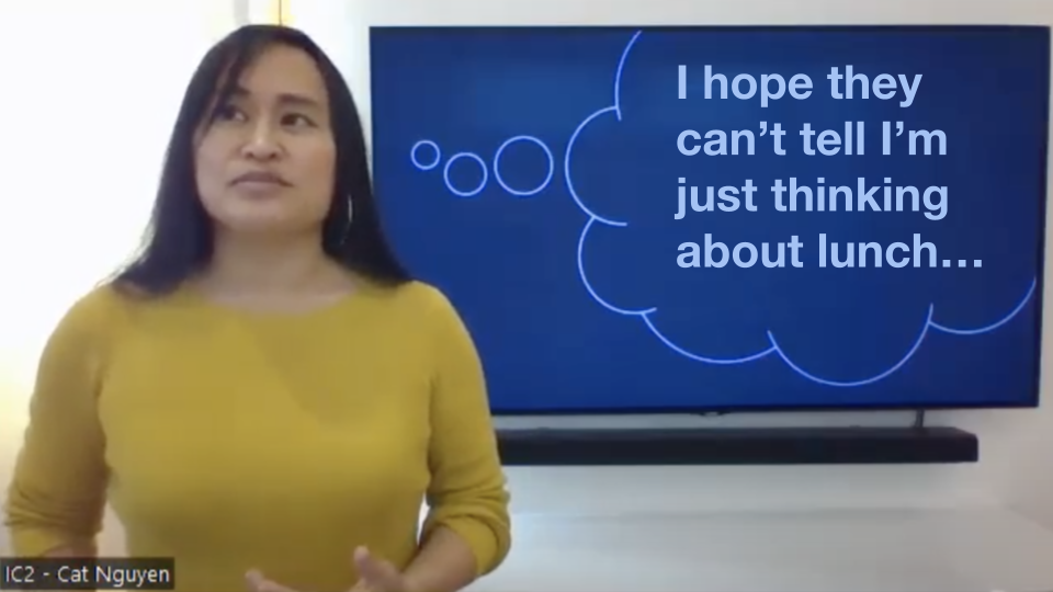 Video still of Vietnamese-American woman delivering a speech and looking up and to her right, standing to the left of a TV screen behind her. On the TV screen is a slide with a thought bubble image that makes it look like she's thinking the text, "I hope they can’t tell I’m just thinking about lunch…"